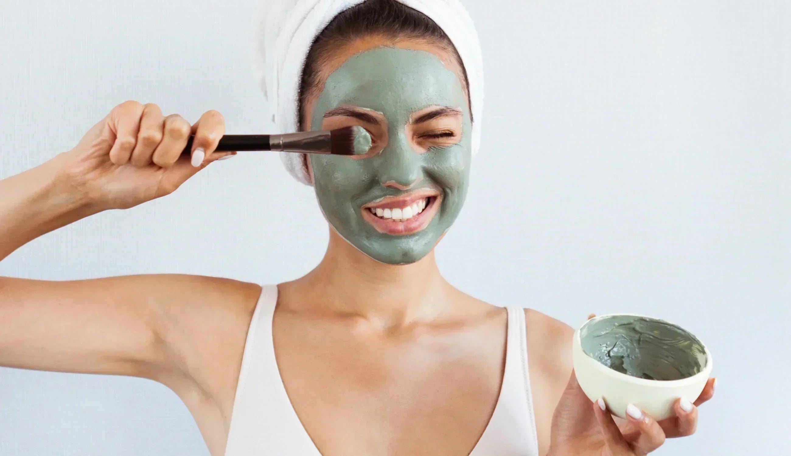 A woman applying a clay mask to her face, demonstrating how to use clay masks for skincare