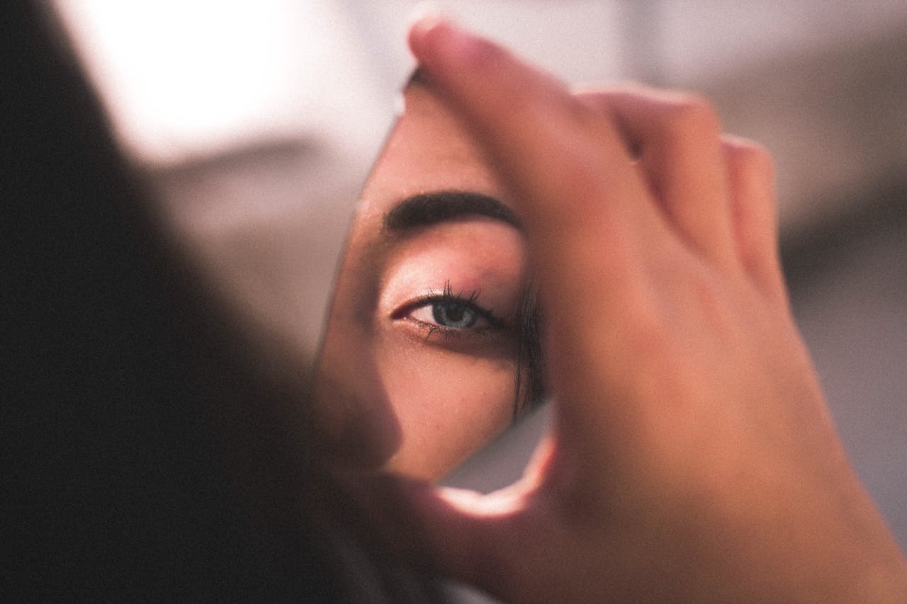 woman looking at her face in a piece of broken mirror