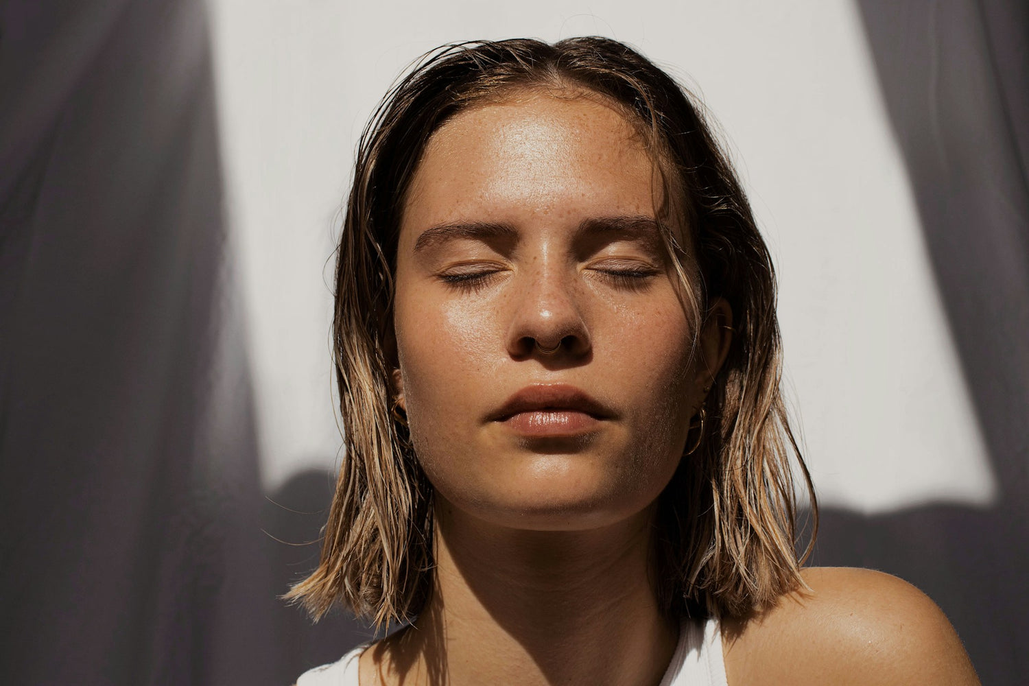 Woman with glowing skin and closed eyes standing in bright sunlight